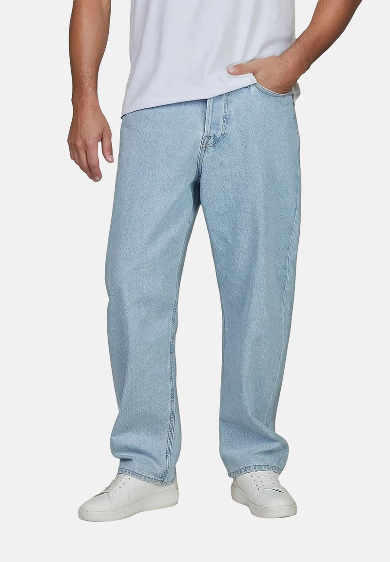 Pantalones de mezclilla azul claros con un corte holgado, con cremallera, bolsillos laterales y un diseño de pierna recta, combinados con zapatillas blancas.