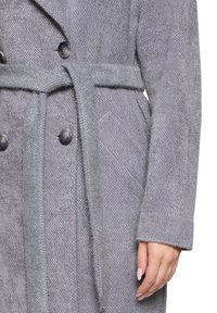 Manteau en mélange de laine grise avec une finition texturée, design croisé, ceinture et poches latérales. Les boutons notables sont gris foncé.