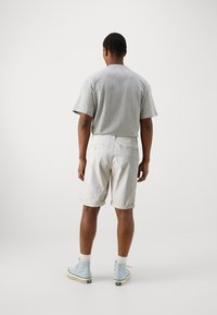 Camiseta gris de manga corta combinada con pantalones cortos beige claros remangados. Presenta un corte relajado y está hecha de una tela suave. Zapatillas altas azules.