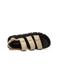 Beige suede sandal with three wide straps, black textured sole, and adjustable ankle strap featuring gold-tone hardware.
