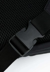 Lähedalt vaadatuna must plastmassist külgklõpsake ja musta kudumisega rihma, samuti võrgukanga taust.