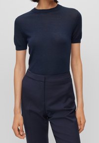 Marinblå kortärmad stickad topp med rund halsringning. Mjuk textur och lätt genomskinlighet, kombinerat med högmidjade marinblå byxor.