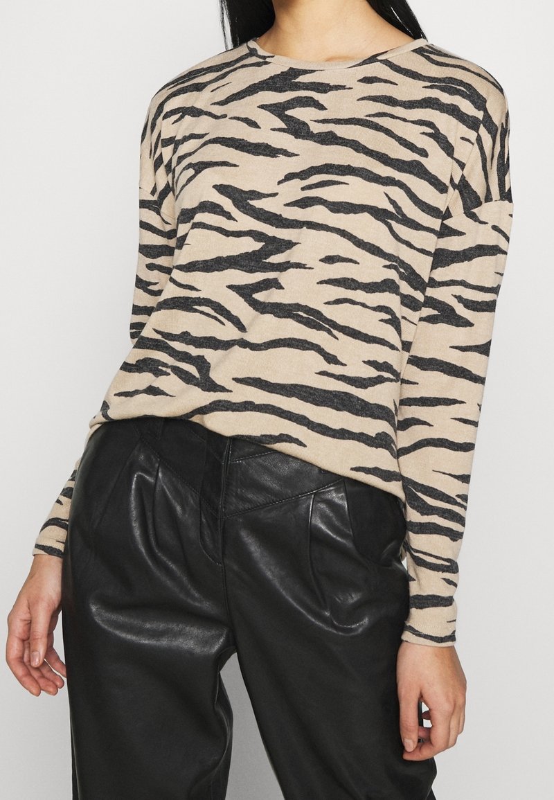 Beige Pullover mit schwarzen Tigerstreifen, Rundhalsausschnitt und langen Ärmeln, kombiniert mit schwarzen Lederhosen. Weicher Stoff.