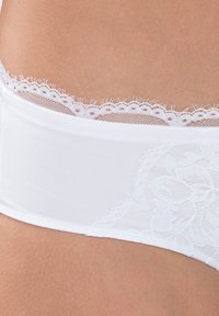 Witte ondergoed van een gladde stof, met een kanten tailleband met golvende randen en bloemenkantdetail aan de zijkant.