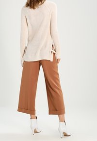 Ljusbeige ribbstickad tröja med sidospjäll, kombinerad med vida bruna byxor och vita ankelstövlar, som visar en avslappnad passform.