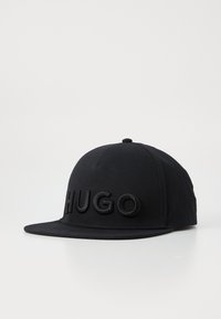 Casquette de baseball noire avec un logo "HUGO" en relief à l'avant, fabriquée en tissu avec une texture lisse et un bord plat.