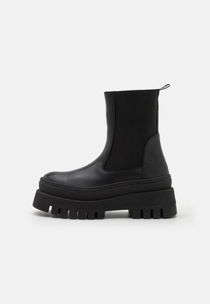 Botte noire à plateforme épaisse mi-mollet avec panneaux latéraux élastiques et languette arrière sur fond blanc.