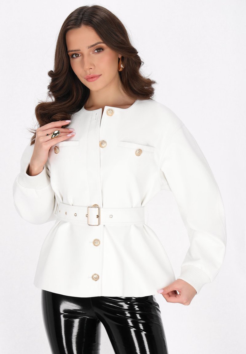 Weißes Peplum-Jackett mit goldenen Knöpfen, strukturierter Kragen und seitlichen Taschen; kombiniert mit schwarzen, glänzenden Hosen; der Stoff wirkt glatt und tailliert.