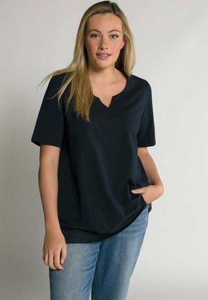Top nero a V con maniche corte, texture morbida, vestibilità ampia e tasca laterale, abbinato a jeans in denim azzurro chiaro.