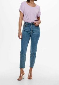 Haut violet clair à manches courtes associé à un jean taille haute bleu ; le jean a une coupe droite et des ourlets effilochés, complété par des talons transparents.