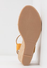 Semelle d'une sandale compensée jaune avec semelle extérieure en caoutchouc texturé, plateforme en jute tressée et bride à la cheville, taille 37.