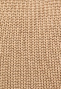 Nahaufnahme von beigem gestricktem Stoff mit einem engen, einheitlichen Rippenmuster und sichtbarer Garnstruktur.