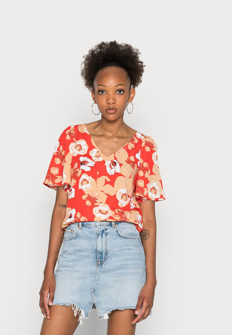 Blusa floral vermelha com mangas curtas e evasê e decote em V. Combinada com uma saia mini de ganga azul clara com detalhes em bainha desfiada.