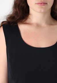 Top senza maniche nero con scollatura rotonda; texture liscia; design minimalista senza motivi o accenti aggiuntivi.