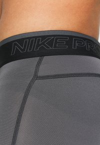 Pantalones cortos deportivos grises con una cintura elástica negra que presenta la marca "NIKE PRO". El tejido es suave y tiene costuras visibles.