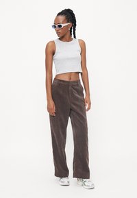 Grijze cropped tanktop en bruine corduroy wide-leg broek. Model draagt witte zonnebril en sneakers met reflecterende accenten.