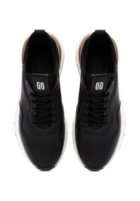 Zwarte sneakers met een gladde leren bovenkant, een witte rubberen zool en zwarte veters. Kenmerkt zich door een logo op de tong en een gewatteerde enkel.