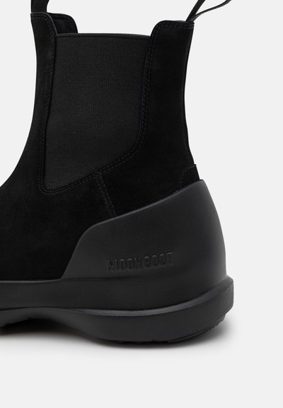 Fekete bokacipő, velúrbőr felsőrésszel, rugalmas oldalpanelokkal és текстúrázott gumitalppal. A saroknál "MOON BOOT" felirat.