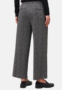 Persona che indossa pantaloni a gamba larga grigi a vita alta con un motivo a spina di pesce nero e mocassini neri, mostrata di spalle.