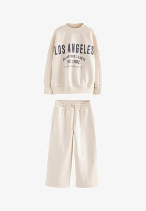 Kremowy sweatshirt z granatowym napisem "LOS ANGELES CHAMPIONS LEAGUE EST.1982", w połączeniu z pasującymi spodniami dresowymi z elastycznym pasem.