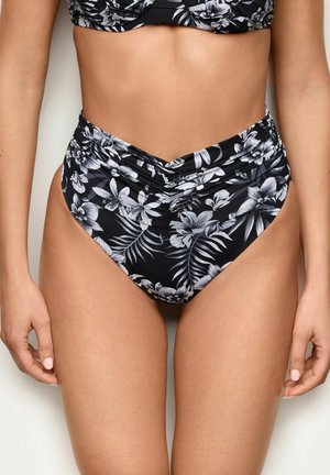 Mujer con braguitas de bikini negras de talle alto con estampado floral blanco y detalle fruncido en la parte delantera, vista desde la cintura hasta los muslos.