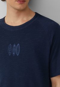 Dunkelblaues Kurzarm-T-Shirt aus strukturiertem Stoff, mit drei hellblauen Surfbrett-Designs, die auf der Brust gestickt sind.