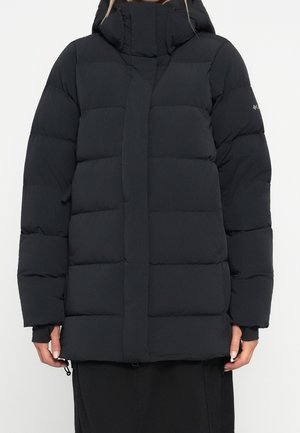 Chaqueta de invierno acolchada negra con cuello alto, mangas largas, cremallera frontal y bolsillos laterales, usada por una persona de pie.