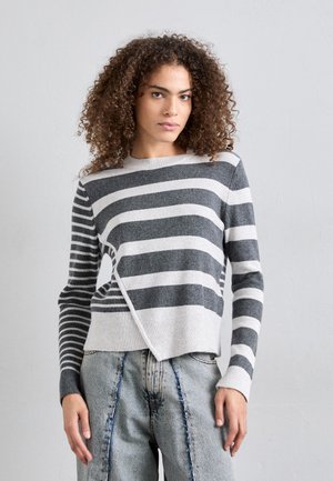 Maglione a righe grigio e bianco. Presenta un colletto rotondo, orlo asimmetrico e un tessuto a maglia testurizzato. Abbinato a jeans chiari, strappati.