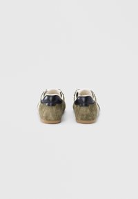 Πράσινα sneakers από σουέντ με μαύρη δερμάτινη λεπτομέρεια στο τακούνι και λευκές τρύπες για τα κορδόνια. Επίπεδη ελαστική σόλα, στρογγυλή μύτη και ραμμένες λεπτομέρειες.