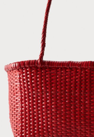Κοντινό πλάνο κόκκινου υφασμένου καλάθι με πλεκτή λαβή σε απλό φωτεινό φόντο.