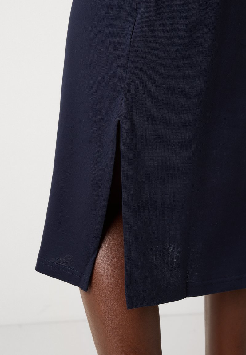 Granatowa sukienka z bocznym rozcięciem, wykonana z gładkiego materiału, z czystą linią dołu oraz dopasowaną sylwetką. Teksturowany wygląd w pobliżu rozcięcia.