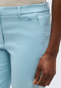 Κοντινό πλάνο ανοιχτό μπλε παντελονιού με πλευρική τσέπη με φερμουάρ, που φοριέται από άτομο με σκούρο δέρμα, δείχνοντας μέρος του χεριού και της μέσης του.