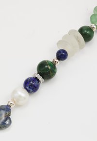 Collar de múltiples cuentas que presenta piedras verdes, azules y blancas, con acentos plateados y formas variadas, incluyendo formas redondas y parecidas a discos.
