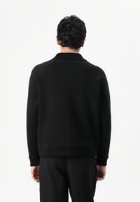 Sudadera de algodón negra con cuello y puños acanalados, con un corte corto y un sutil logo en la parte posterior del cuello.