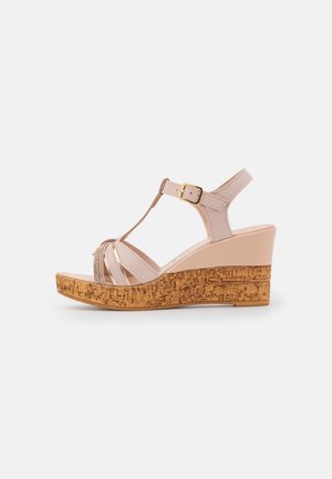 Beige Leder Wedge Sandale mit Korksohle, offener Zeh, T-Riemen-Design und goldener Schnalle auf weißem Hintergrund.