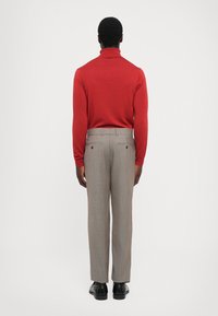 Red turtleneck sweater with ribbed collar paired with light gray plaid trousers, featuring two back pockets and black shoes.