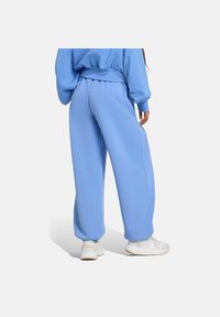 Pantalones jogger de color azul claro, hechos de una tela suave, con un corte relajado, cintura elástica y puños en los tobillos. Combinados con zapatillas blancas.