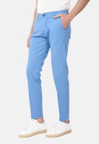 Pantaloni slim-fit azzurri realizzati in cotone, con frontale piatto, tasche e chiusura con bottone, abbinati a sneaker bianche.
