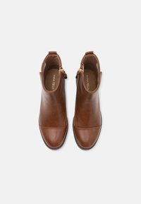 Botines de cuero marrón con una textura suave, punta redonda, cremallera lateral y un detalle de costura mínima. Diseño clásico con un tacón bajo.