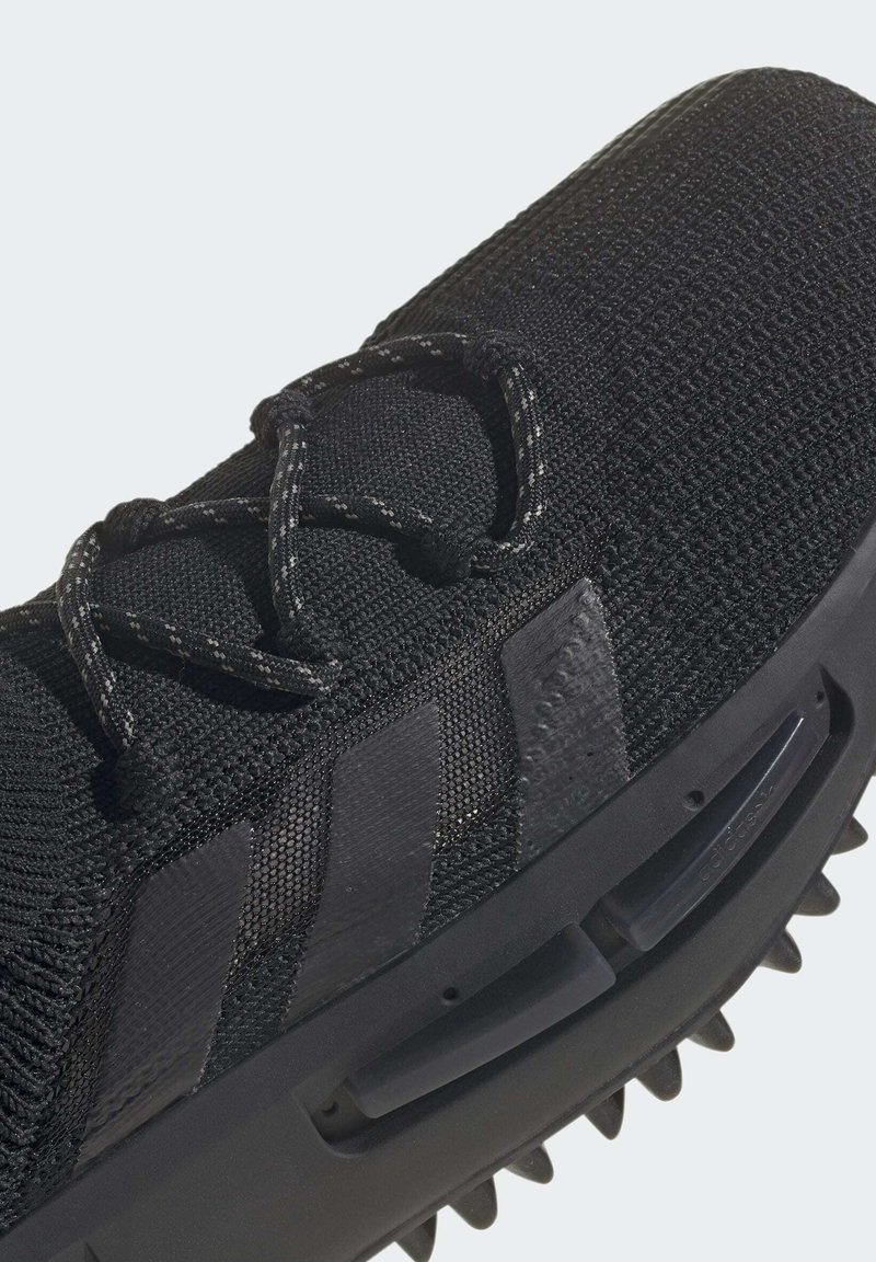 Zapatilla deportiva negra con un upper de punto texturizado, cordones tonales, tres rayas negras y una suela con tachuelas para mayor tracción.