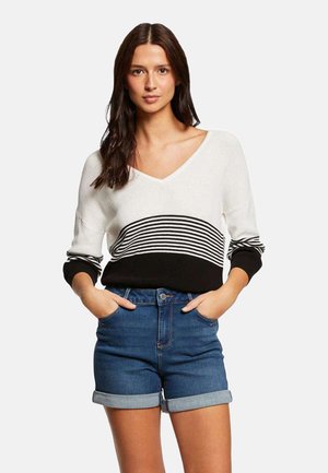 Maglione a maglia con scollo a V, caratterizzato da strisce orizzontali bianche e nere, abbinato a pantaloni shorts in denim. Tessuto morbido, vestibilità rilassata e maniche arrotolate.