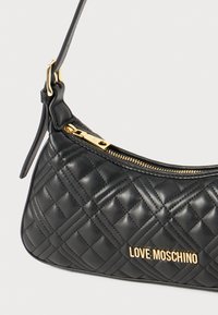 Black quilted leather shoulder bag with gold hardware and zip closure. Features embossed pattern and a logo plate on the front.