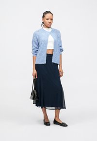 Γαλάζια πλεκτή ζακέτα, λευκό crop top, μακρύ σκούρο μπλε φούστα, μαύρα μπαλαρίνες και μικρή μαύρη τσάντα. Μαλακή υφή και άνετη εφαρμογή.