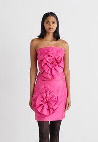 Rosa stroppeløs topp med store blomstaccents, kombinert med et matchende skjørt som har lignende blomstermønstre, satt mot en nøytral bakgrunn.
