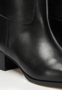 Czarne skórzane botki za kostkę o gładkiej fakturze, zaokrąglonym nosku i niskim, blokowym obcasie. Widoczne przeszycia wzdłuż szwów.