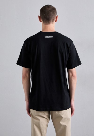 T-shirt en coton noir à manches courtes, arborant un logo "MOSCHINO" blanc dans le dos. Présenté sur un mannequin de dos.