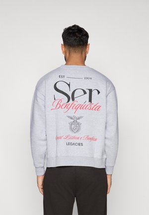 Light gray sweatshirt with a loose fit, featuring large black text and red accents. Contains a logo with an eagle and the text "Sport Lisboa e Benfica."