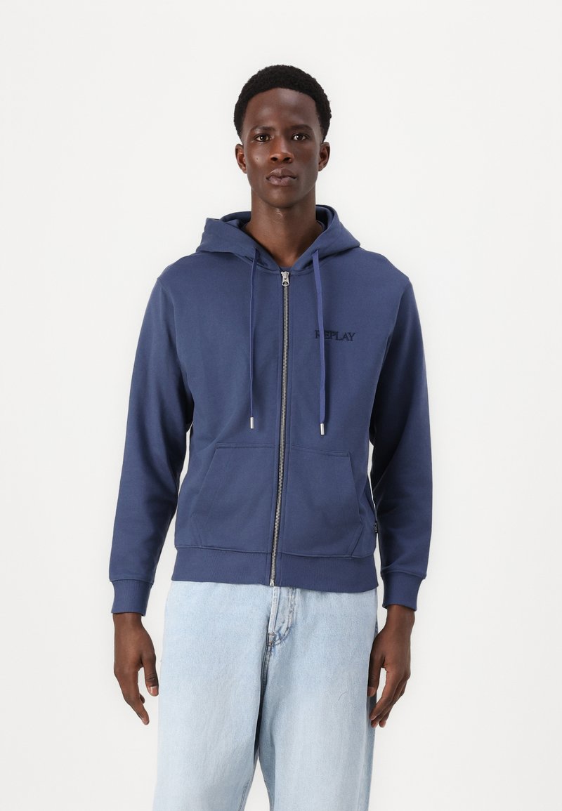 Marineblå zip-hoodie lavet af bomuldsblanding, med en frontlomme, snor i hætten og broderet logo på brystet.