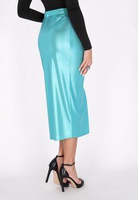 En metallisk teal midi kjol med en slät textur, paired med svarta remsandaler med klack, som visar upp en figursydd midja och en subtil glans.