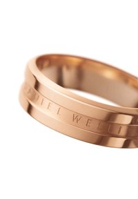 Vaaleanpunakultainen metallirengas, jossa on sileä pinta ja kaiverrettu "DANIEL WELLINGTON" ympäri rengasta. Rengas esittää kaksiraidallista muotoilua.